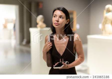 Woman with phone in hands in museum hall, view statues exhibition. Woman with phone in hands in museum hall, view statues exhibition. 141065186