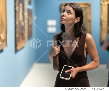 Woman visiting museum and looking at paintings in gold frames Woman visiting museum and looking at paintings in gold frames 141065249