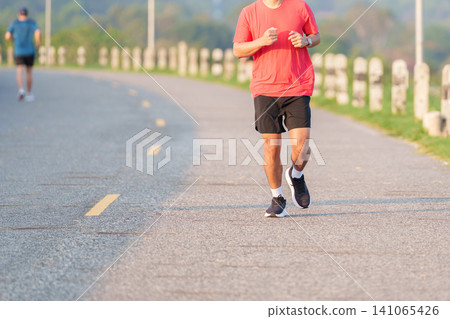 Active young Asian man jogging and running in the public park at morning. Male athlete in sportswear exercising for healthy lifestyle and fitness workout outdoors. Wellness and sport concepts Active young Asian man jogging and running in the public park at morning. Male athlete in sportswear exercising for healthy lifestyle and fitness workout outdoors. Wellness and sport concepts 141065426