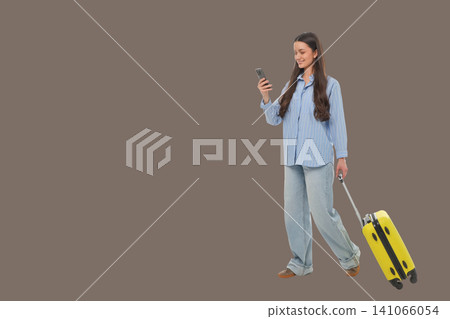 Woman walks with a suitcase while using her mobile device Woman walks with a suitcase while using her mobile device 141066054