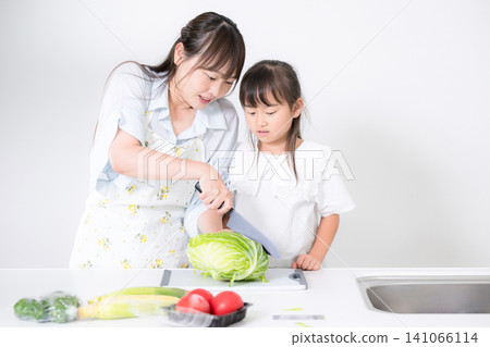 A mother and her elementary school-aged and preschool-aged daughters learn how to use a knife through cooking in the kitchen. A mother and her elementary school-aged and preschool-aged daughters learn how to use a knife through cooking in the kitchen. 141066114