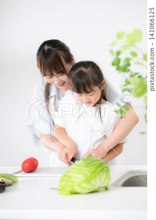 一位母親和她上小學和上幼兒園的女兒們在廚房裡透過烹飪學習如何使用刀具。 一位母親和她上小學和上幼兒園的女兒們在廚房裡透過烹飪學習如何使用刀具。 141066125