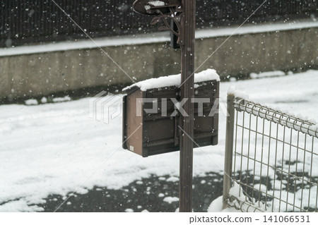 An antique-style mailbox covered in snow stands amidst a heavy snowfall. An antique-style mailbox covered in snow stands amidst a heavy snowfall. 141066531