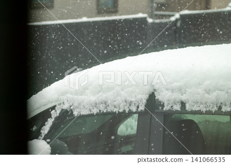 A white car with snow piled on its roof due to heavy snowfall, and a landscape of continuously falling snow. A white car with snow piled on its roof due to heavy snowfall, and a landscape of continuously falling snow. 141066535