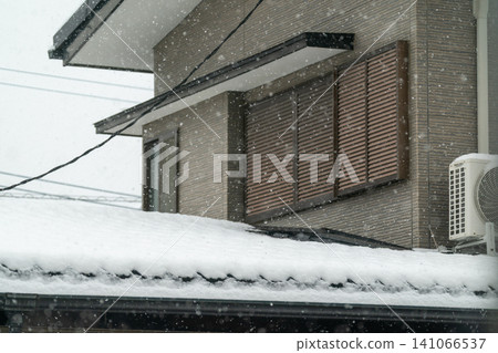 A detached house with its second-floor shutters closed on a snowy day. A detached house with its second-floor shutters closed on a snowy day. 141066537