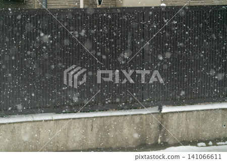 A snowy landscape of a fence and concrete wall with fine snow continuously falling. A snowy landscape of a fence and concrete wall with fine snow continuously falling. 141066611