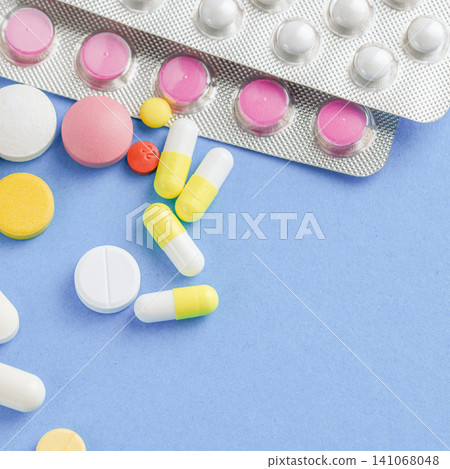 Colorful medical tablets and capsules spilled from a blister pack on blue surface Colorful medical tablets and capsules spilled from a blister pack on blue surface 141068048