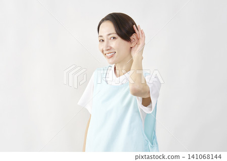 A female caregiver with her hand to her ear against a white background. A female caregiver with her hand to her ear against a white background. 141068144
