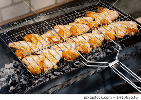 BBQ picnic time Roasted chicken legs and wings on grill. Grilling meat on outdoor grill grid tasty barbeque chicken steak with smoke flames juicy meat in the backyard BBQ picnic time Roasted chicken legs and wings on grill. Grilling meat on outdoor grill grid tasty barbeque chicken steak with smoke flames juicy meat in the backyard 141068630