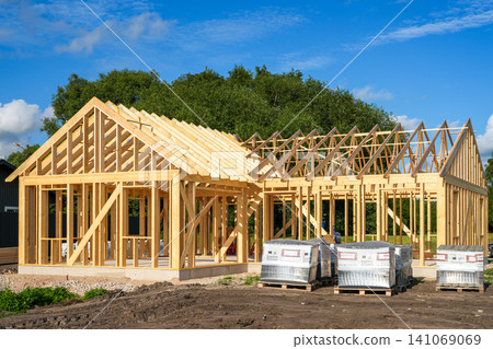 Modern Timber Frame House Under Construction with Wooden Roof Trusses at Residential Building Site Modern Timber Frame House Under Construction with Wooden Roof Trusses at Residential Building Site 141069069