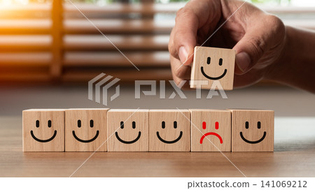 Close up of a hand choosing a happy smile face wooden block to replace a red sad face. A concept of customer service evaluation, satisfaction survey, review, and positive mindset Close up of a hand choosing a happy smile face wooden block to replace a red sad face. A concept of customer service evaluation, satisfaction survey, review, and positive mindset 141069212