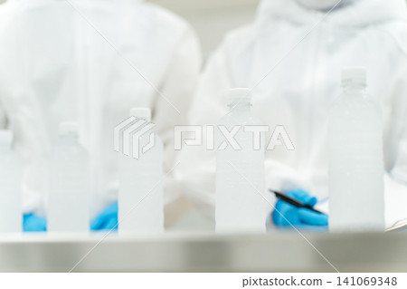 A production staff member in a dustproof suit checking bottled water at a water factory and beverage manufacturer (beverage manufacturer) A production staff member in a dustproof suit checking bottled water at a water factory and beverage manufacturer (beverage manufacturer) 141069348