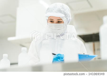 A production staff member in a dustproof suit checking bottled water at a water factory and beverage manufacturer (beverage manufacturer) 141069349