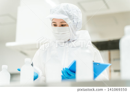 A production staff member in a dustproof suit checking bottled water at a water factory and beverage manufacturer (beverage manufacturer) 141069350