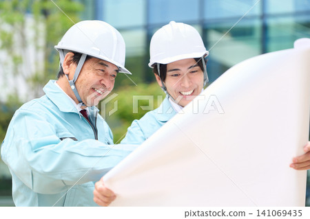 An Asian site supervisor giving instructions while looking at blueprints. An Asian site supervisor giving instructions while looking at blueprints. 141069435