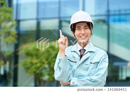 An Asian man in work clothes points his finger. 141069451