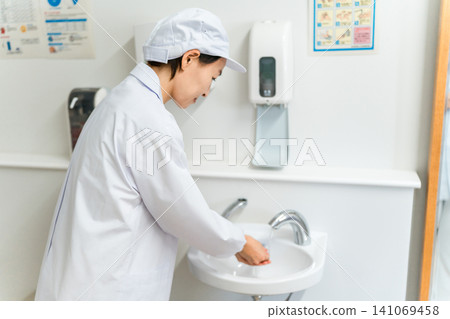 Female factory staff wearing food-related white coats and cleanroom wear washing their hands. Female factory staff wearing food-related white coats and cleanroom wear washing their hands. 141069458
