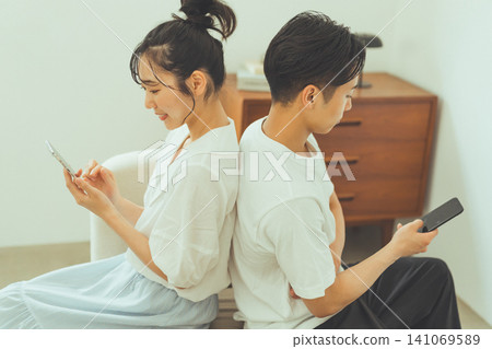 A couple standing back-to-back, staring at their smartphones. A couple standing back-to-back, staring at their smartphones. 141069589