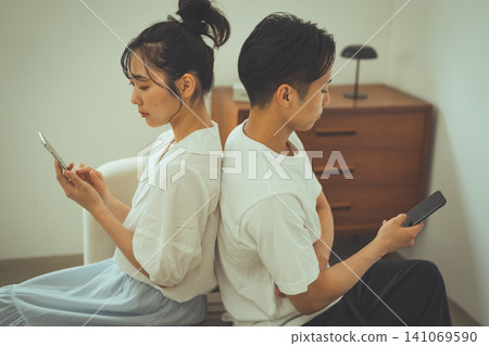 A couple, each looking at their smartphones, back to back. A couple, each looking at their smartphones, back to back. 141069590