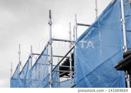 A view looking up at scaffolding at a construction site, covered with blue protective sheets. A view looking up at scaffolding at a construction site, covered with blue protective sheets. 141069684