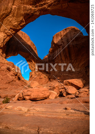 Majestic natural rock arch formation framing bright blue sky in an awe inspiring peaceful red sandstone utah desert landscape showcasing magnificent geological wonder 141069725