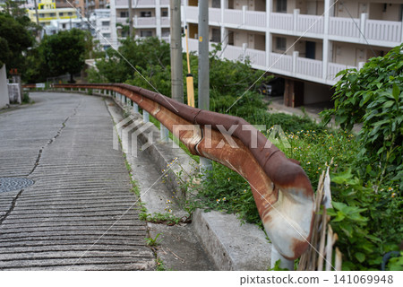 A rusty guardrail, partially deformed from being hit, installed on a slope. A rusty guardrail, partially deformed from being hit, installed on a slope. 141069948