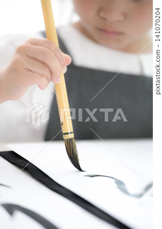 特寫鏡頭拍攝了一名沒有面孔的小學生學習書法時,專注地用毛筆寫字的雙手。 特寫鏡頭拍攝了一名沒有面孔的小學生學習書法時,專注地用毛筆寫字的雙手。 141070204