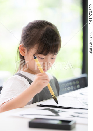 A close-up of a young elementary school girl concentrating on calligraphy, writing characters with a brush. Japanese children learning calligraphy, with serious expressions. A close-up of a young elementary school girl concentrating on calligraphy, writing characters with a brush. Japanese children learning calligraphy, with serious expressions. 141070209
