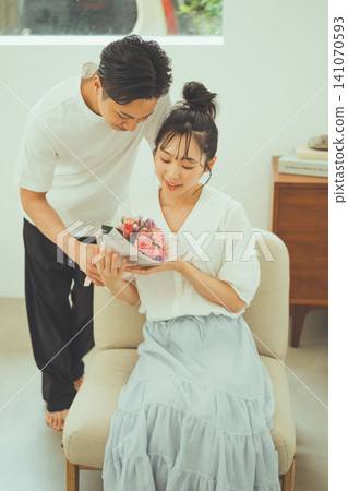 A woman smiles as she receives a bouquet of flowers, while a male couple peers in. A woman smiles as she receives a bouquet of flowers, while a male couple peers in. 141070593