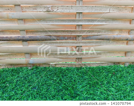 Bamboo woven fence background with green artificial grass foreground. 141070794