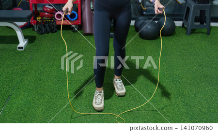 Cropped view of woman jumping rope on green turf in gym for cardio workout Cropped view of woman jumping rope on green turf in gym for cardio workout 141070960
