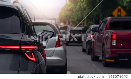 Vehicles gridlocked in heavy traffic on an urban highway. Red brake lights flare across the long rows of cars during a busy evening sunlight is soft commute. Side road with trees pleasant atmosphere. Vehicles gridlocked in heavy traffic on an urban highway. Red brake lights flare across the long rows of cars during a busy evening sunlight is soft commute. Side road with trees pleasant atmosphere. 141071092