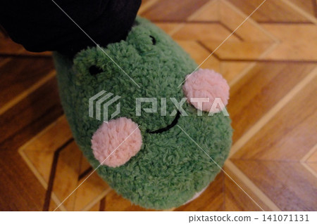 Cute green slippers, a plush frog with pink cheeks sits on the parquet floor Cute green slippers, a plush frog with pink cheeks sits on the parquet floor 141071131