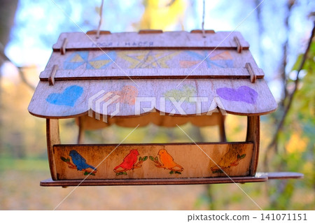Handcrafted wooden bird feeder suspended outdoors in a park Handcrafted wooden bird feeder suspended outdoors in a park 141071151