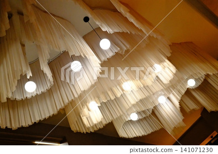 Cream fabric layers drape from the ceiling, lit by bright spherical pendant lights Cream fabric layers drape from the ceiling, lit by bright spherical pendant lights 141071230