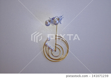 Elegant gold pearl spiral earring on light gray, highlighting details Elegant gold pearl spiral earring on light gray, highlighting details 141071239