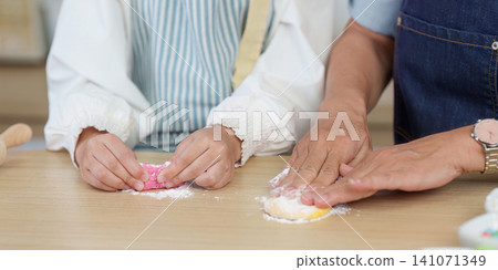 Cropped hands of adult and child kneading colorful dough on wooden table Cropped hands of adult and child kneading colorful dough on wooden table 141071349