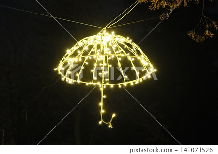 Yellow string lights form an illuminated umbrella hanging outdoors from branches at night Yellow string lights form an illuminated umbrella hanging outdoors from branches at night 141071526