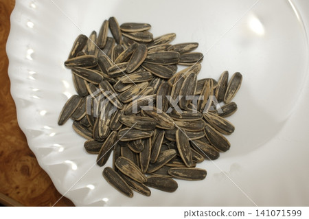 Many striped black and white sunflower seeds fill a white ceramic plate. Many striped black and white sunflower seeds fill a white ceramic plate. 141071599