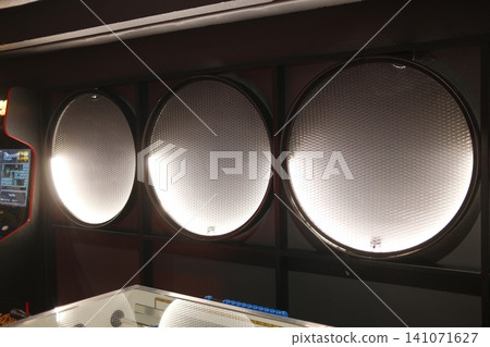 Three large round lights with a honeycomb surface illuminate a dark arcade room Three large round lights with a honeycomb surface illuminate a dark arcade room 141071627