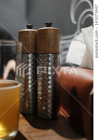Two decorative, hammered metal/wood pepper grinders, beer, tissue box on rustic table 141071647