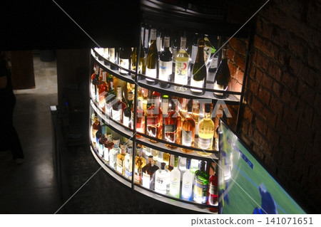 Dark bar: backlit bottles, sleek curved bar, brick wall, TV playing a game 141071651
