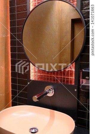 Modern restroom: round mirror, wall faucet, oval sink, warm orange grid lighting Modern restroom: round mirror, wall faucet, oval sink, warm orange grid lighting 141071663
