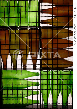 Green and amber glass bottles fill a black wire grid indoors. Green and amber glass bottles fill a black wire grid indoors. 141071666