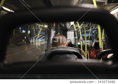 Nighttime travel inside a public transport bus with a person sitting from the back on an evening commute Nighttime travel inside a public transport bus with a person sitting from the back on an evening commute 141071686