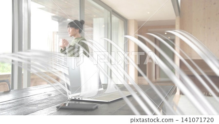 Holding mug, woman in green sweater gazing through glass doors at home, laptop visible, copy space Holding mug, woman in green sweater gazing through glass doors at home, laptop visible, copy space 141071720