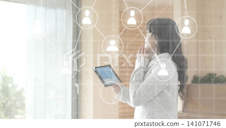 Holding woman wearing light gray sweater touching chin while viewing tablet near glass door overlay Holding woman wearing light gray sweater touching chin while viewing tablet near glass door overlay 141071746