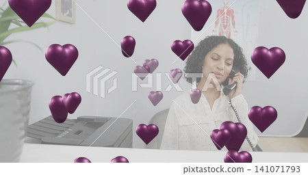 Answering receptionist wearing white blouse holding corded phone behind desk with purple hearts Answering receptionist wearing white blouse holding corded phone behind desk with purple hearts 141071793