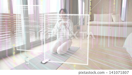 Kneeling woman in light hoodie, sweats meditating on yoga mat in room, smartphone and AR overlays Kneeling woman in light hoodie, sweats meditating on yoga mat in room, smartphone and AR overlays 141071807