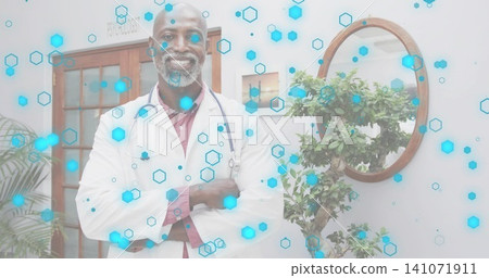 Smiling doctor standing in center of clinic room, wearing lab coat, stethoscope, blue hex overlay Smiling doctor standing in center of clinic room, wearing lab coat, stethoscope, blue hex overlay 141071911